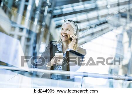 Stock Photography - Caucasian businesswoman talking on cell phone leaning on railing in lobby. Fotosearch