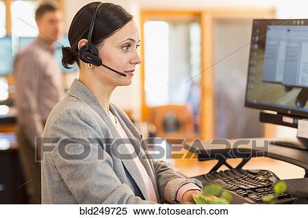 Stock Photography - Caucasian businesswoman wearing headset using computer. Fotosearch