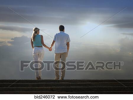 Stock Image - Caucasian couple admiring scenic view of clouds from staircase. Fotosearch