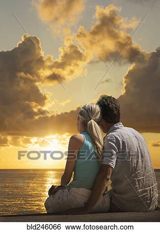 Stock Photograph - Caucasian couple admiring scenic view of sunset at ocean. Fotosearch