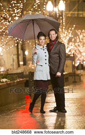 Caucasian couple carrying umbrella in city at night View Large Photo Image Stock Photo - Caucasian couple carrying umbrella in city at night. Fotosearch