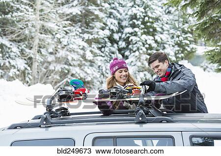 Stock Image - Caucasian couple checking snowboards in car roof rack. Fotosearch