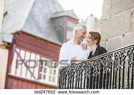 Stock Image - Caucasian couple drinking coffee on balcony in city. Fotosearch