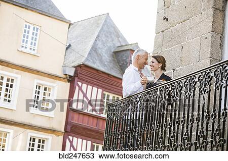 Stock Image - Caucasian couple drinking coffee on balcony in city. Fotosearch