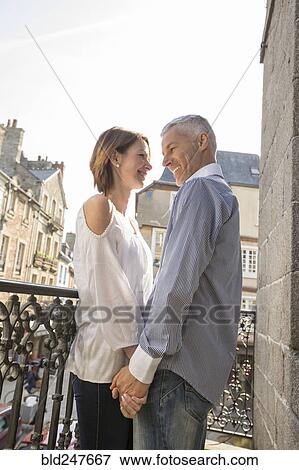 Stock Photo - Caucasian couple holding hands on balcony in city. Fotosearch