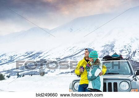 Stock Image - Caucasian couple hugging and leaning on car in winter. Fotosearch