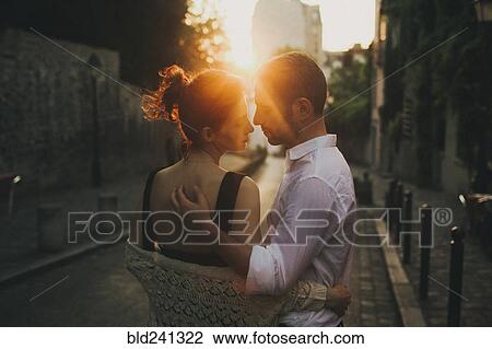 Stock Image - Caucasian couple hugging in city street at sunset. Fotosearch