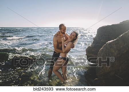 Stock Image - Caucasian couple hugging in ocean. Fotosearch
