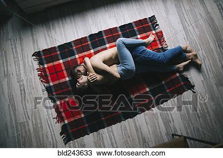 Stock Image - Caucasian couple laying on plaid blanket and hugging. Fotosearch