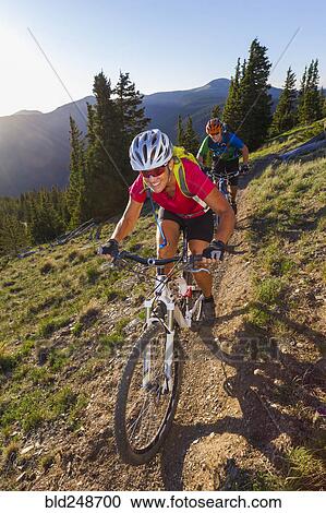 Stock Image - Caucasian couple mountain biking on trail. Fotosearch