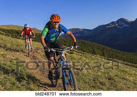 Stock Image - Caucasian couple mountain biking on trail. Fotosearch