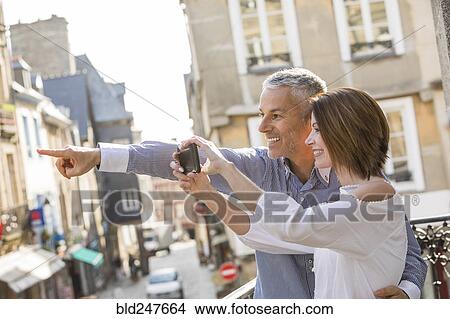 Picture - Caucasian couple photographing with cell phone in city. Fotosearch