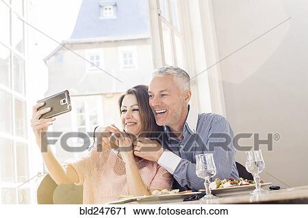 Stock Image - Caucasian couple posing for cell phones selfie in restaurants. Fotosearch