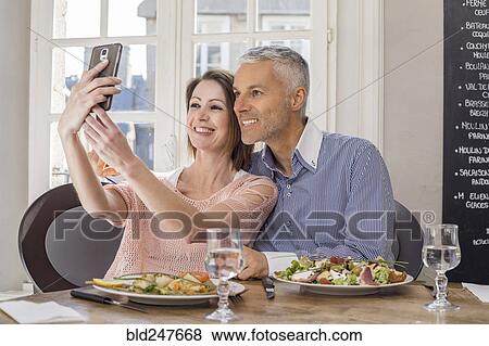 Stock Photo - Caucasian couple posing for cell phones selfie in restaurant. Fotosearch