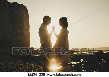 Stock Photography - Caucasian couple pressing hands on beach at sunset. Fotosearch