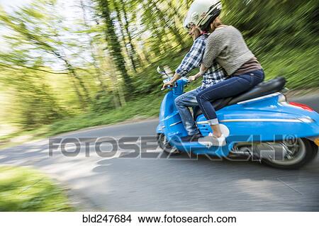 Picture - Caucasian couple riding blue motor scooter. Fotosearch