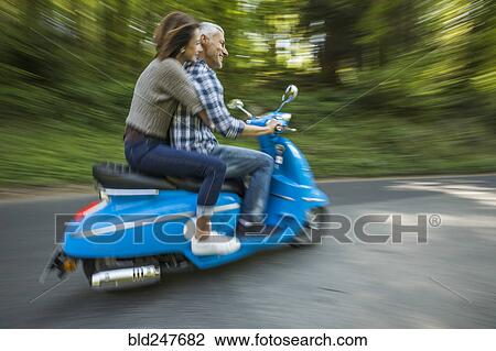 Stock Image - Caucasian couple riding blue motor scooter. Fotosearch