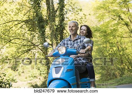 Stock Photo - Caucasian couple riding blue motor scooter. Fotosearch
