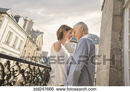 Stock Photograph - Caucasian couple rubbing your noses on balcony in city. Fotosearch