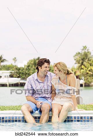 Picture - Caucasian couple sitting at the edge of swimming pool. Fotosearch