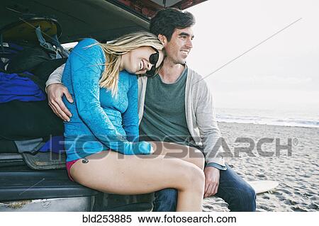 Stock Photography - Caucasian couple sitting in car hatch at beach. Fotosearch