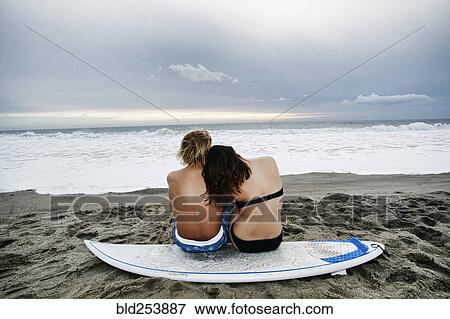 Stock Photo - Caucasian couple sitting on surfboard at beach. Fotosearch