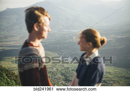 Stock Image - Caucasian couple standing on mountain over valley. Fotosearch