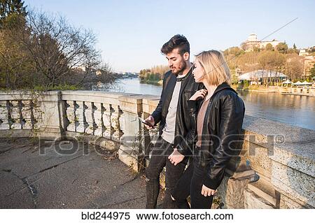 Stock Photography - Caucasian couple texting on cell phone near river. Fotosearch