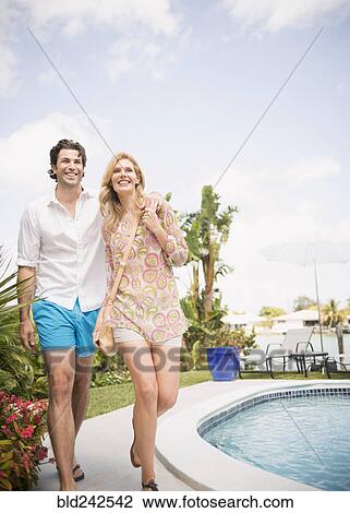 Stock Image - Caucasian couple walking near swimming pool. Fotosearch