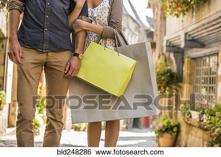 Stock Photograph - Caucasian couple with shopping bags walking in city. Fotosearch