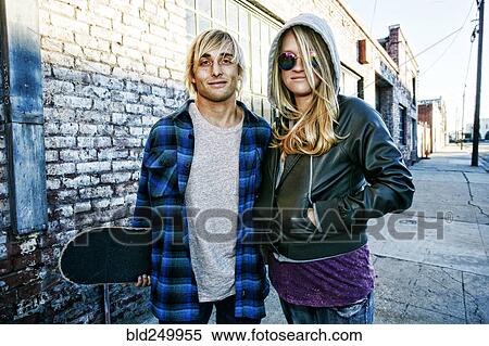 Stock Photography - Caucasian couple with skateboard posing on urban sidewalk. Fotosearch