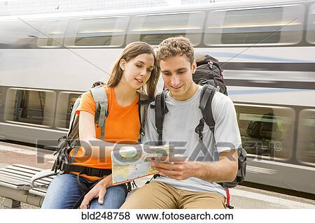 Caucasian couples sitting on bench near train reading map View Large Photo Image Stock Photo - Caucasian couples sitting on bench near train reading map. Fotosearch