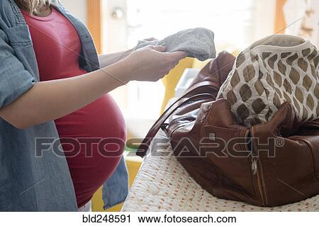 Stock Image - Caucasian expectant mother putting clothing in the bag. Fotosearch