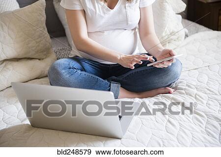 Caucasian expectant mother texting on cell phone on bed View Large Photo Image Stock Photo - Caucasian expectant mother texting on cell phone on bed. Fotosearch