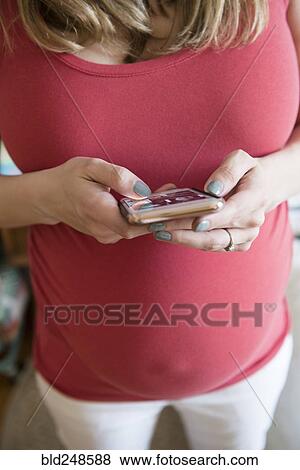 Stock Photo - Caucasian expectant mother texting on cell phone. Fotosearch