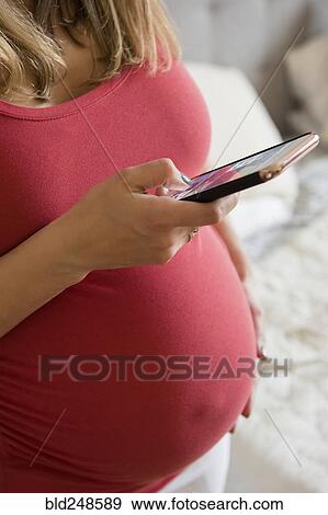 Stock Photo - Caucasian expectant mother texting on cell phone. Fotosearch