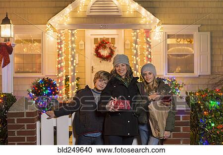 Stock Image - Caucasian family holding Christmas gifts on front stoop. Fotosearch