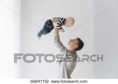 Stock Image - Caucasian father lifting baby son. Fotosearch