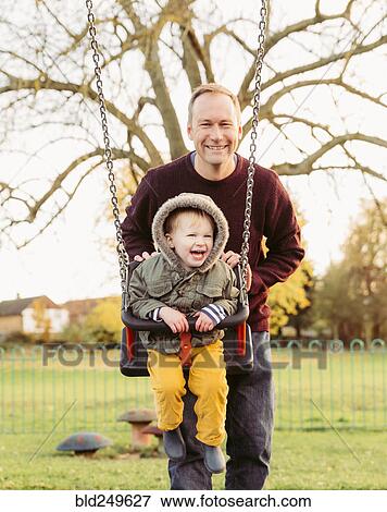 Stock Photo - Caucasian father pushing son on swing. Fotosearch