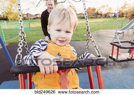 Stock Photograph - Caucasian father pushing son on swing. Fotosearch