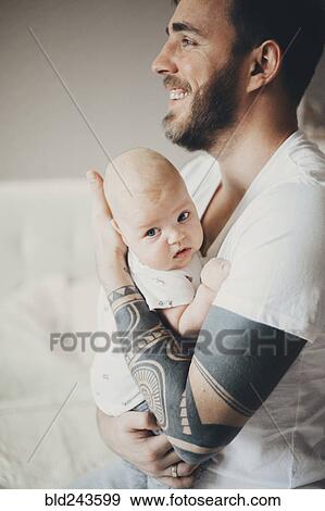 Stock Photo - Caucasian father with tattoos on arms holding baby son. Fotosearch