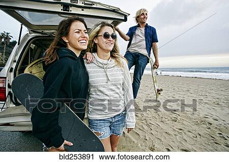 Stock Image - Caucasian friends near car hatch at beach holding skateboards. Fotosearch