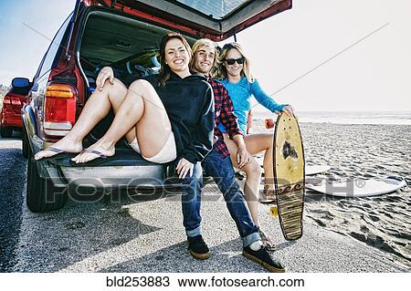 Stock Image - Caucasian friends sitting in car hatch with skateboard. Fotosearch