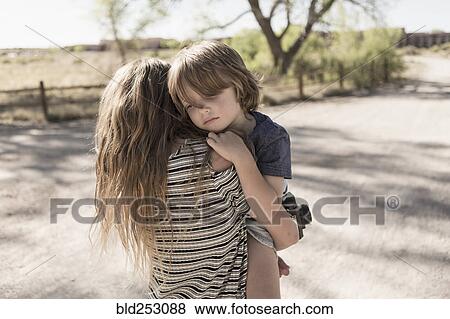 Stock Photo - Caucasian girl carrying brother on dirt path. Fotosearch