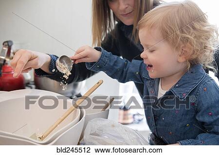 Stock Image - Caucasian girl cooking with mother in kitchen. Fotosearch