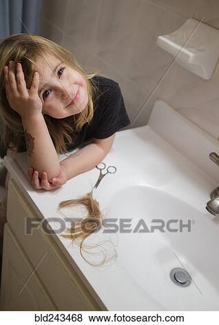 Stock Photo - Caucasian girl cutting her hair in bathroom. Fotosearch