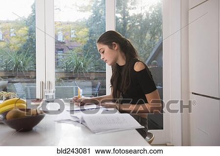 Stock Image - Caucasian girl doing homework in domestic kitchen. Fotosearch
