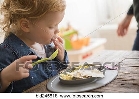 Stock Photo - Caucasian girl eating with fingers and spoon. Fotosearch