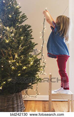 Stock Image - Caucasian girl hanging lights on Christmas tree. Fotosearch