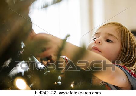 Stock Image - Caucasian girl hanging lights on Christmas tree. Fotosearch